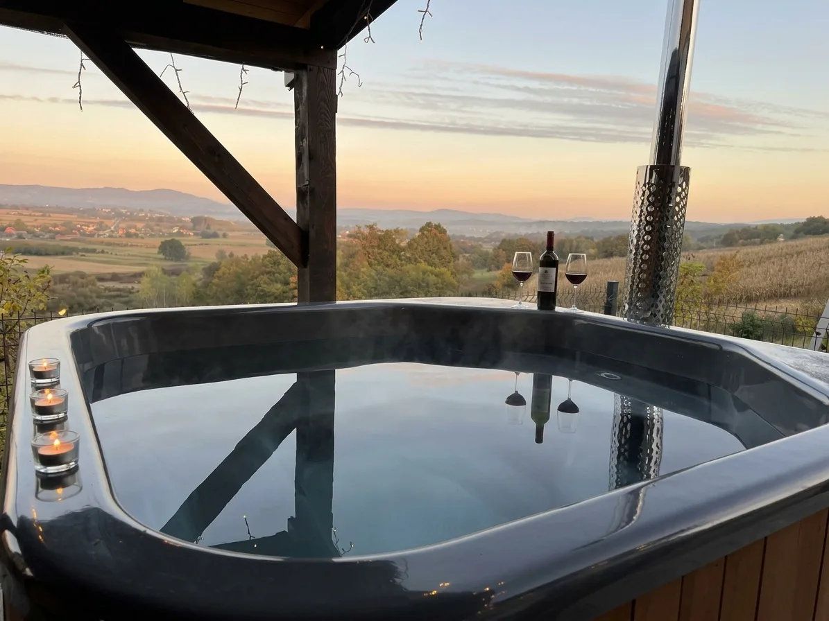 Hot tub pod natkrivenom terasom s pogledom na brežuljke u suton, uz vino i svijeće