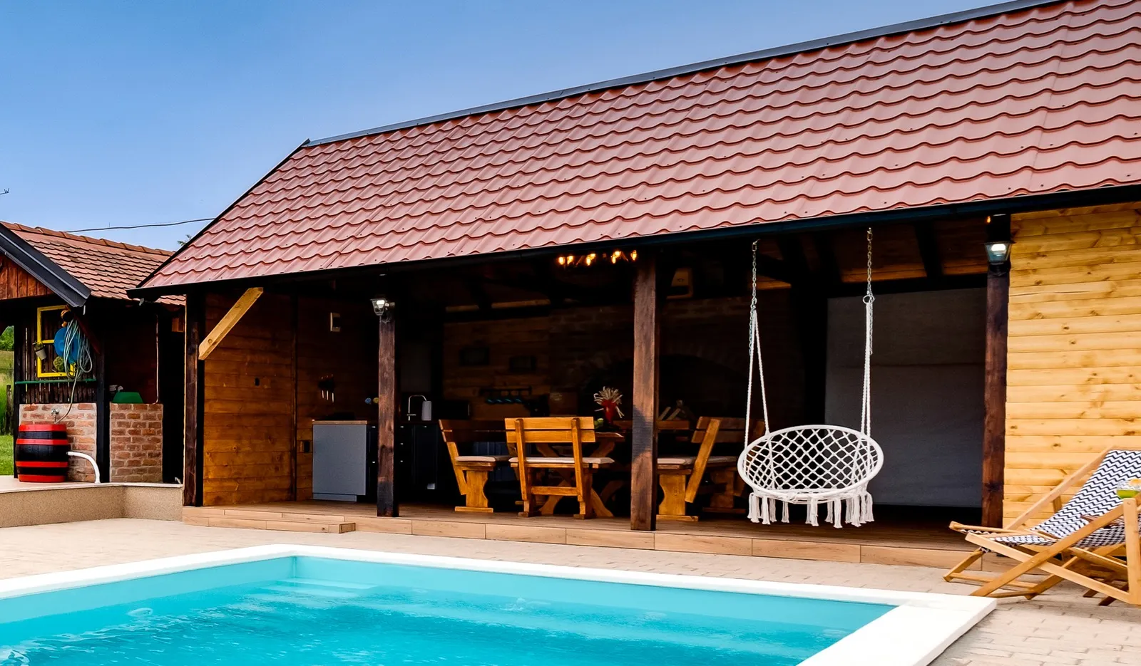 Überdachte Terrasse mit Holztisch, Hollywoodschaukel und Grill